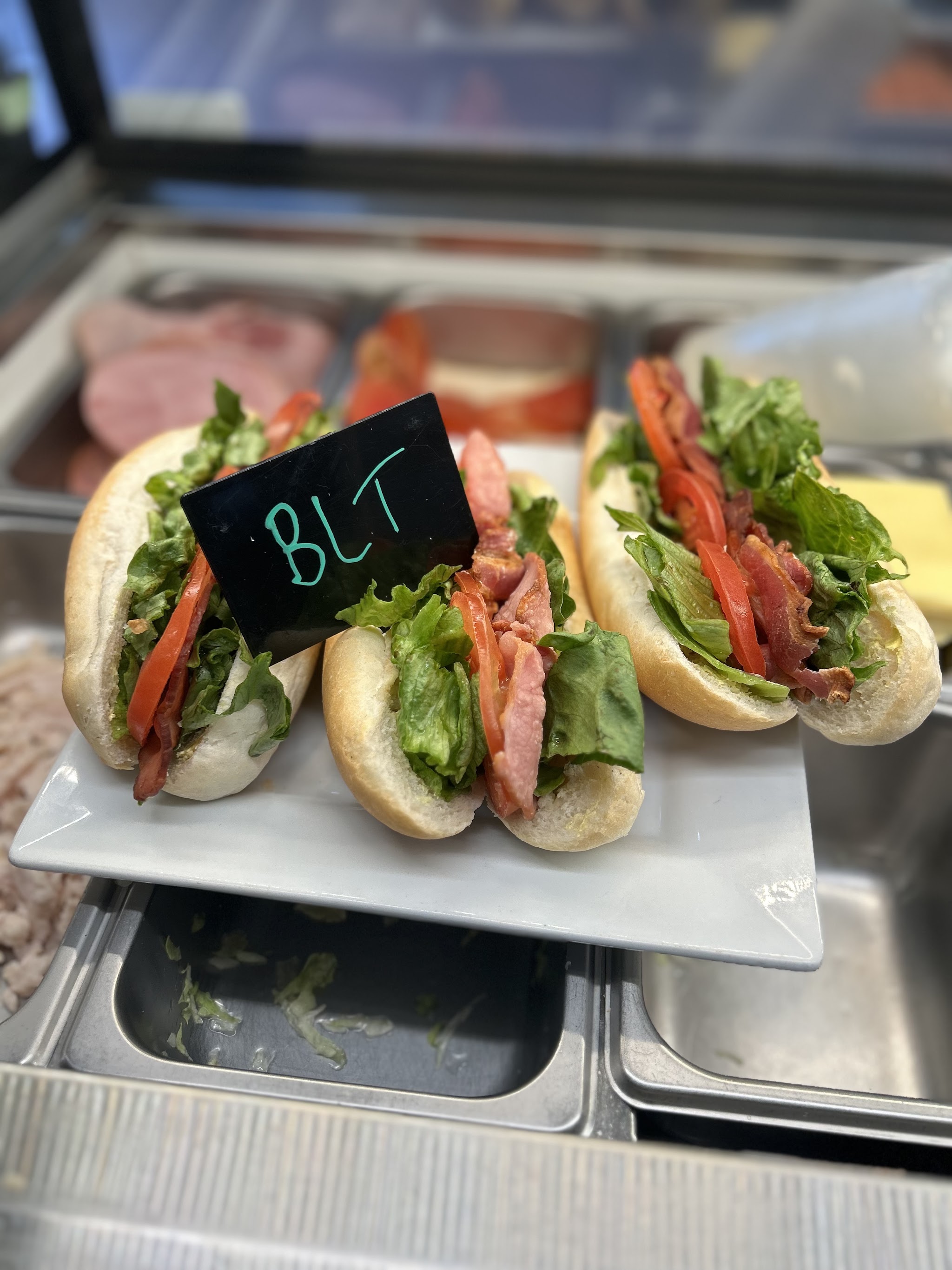 BLT rolls on a display plate in the deli cabinet with a BLT price card
